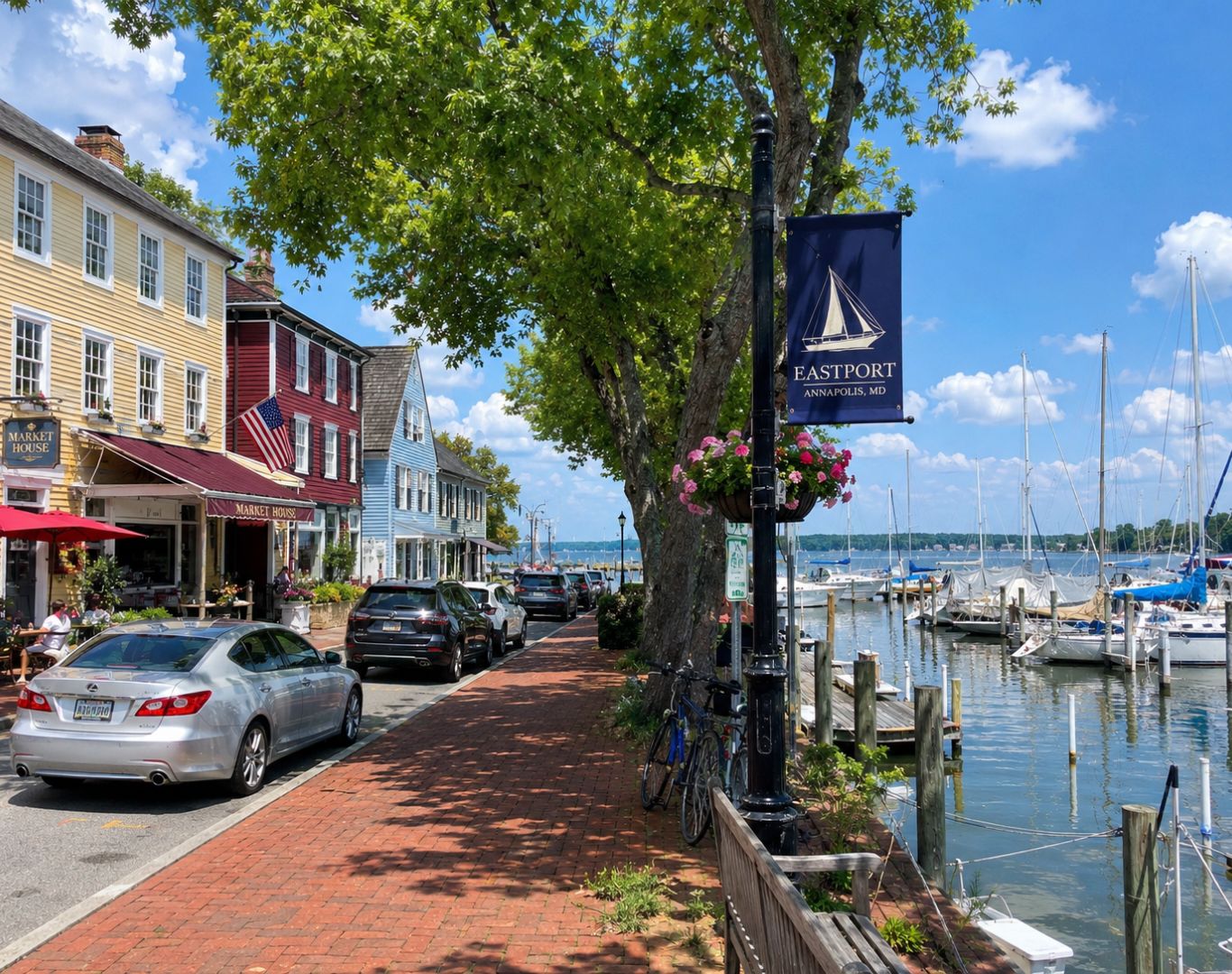 Eastport, MD waterfront street scene with marina sailboats, colorful historic buildings, brick sidewalk, outdoor dining, trees, and an Eastport Annapolis banner